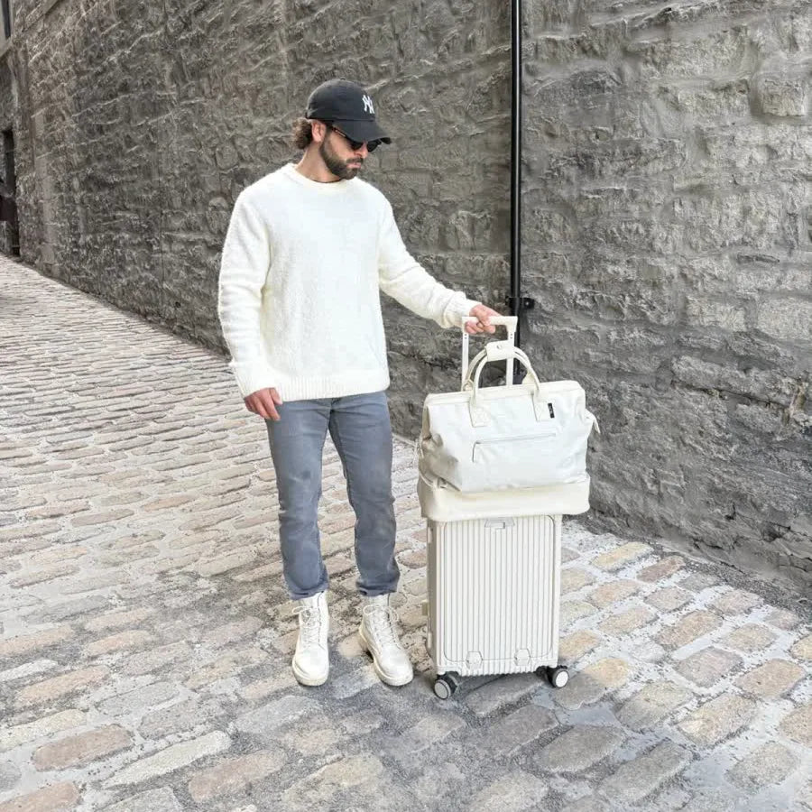 Traveler with a silver NOBL carry-on and weekender on a cobblestone street