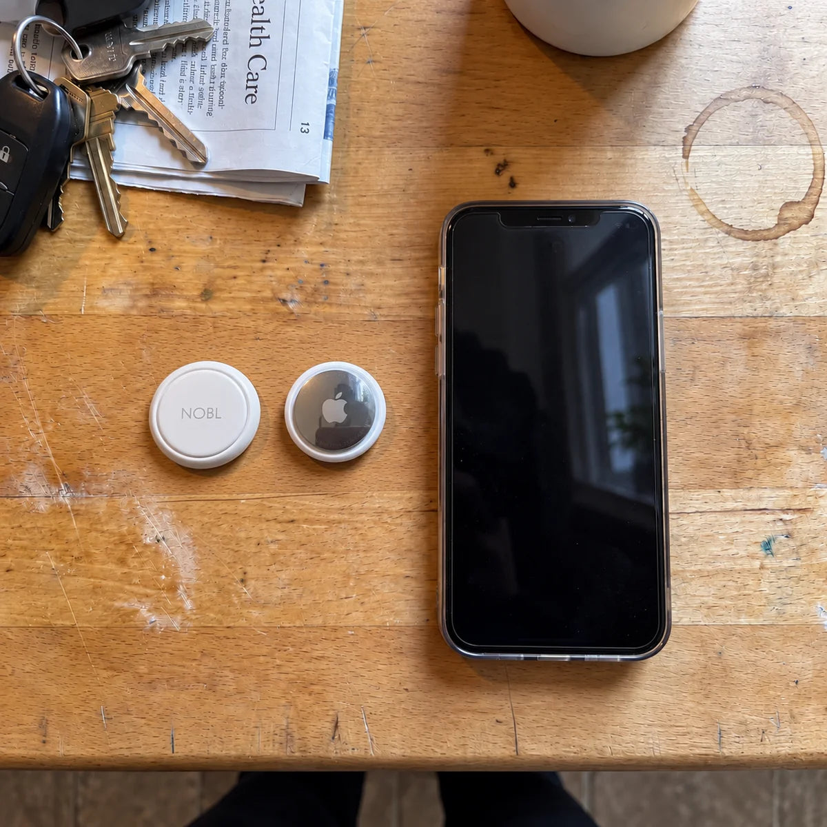 NOBL Air™ and AirTag beside a phone on a wooden table