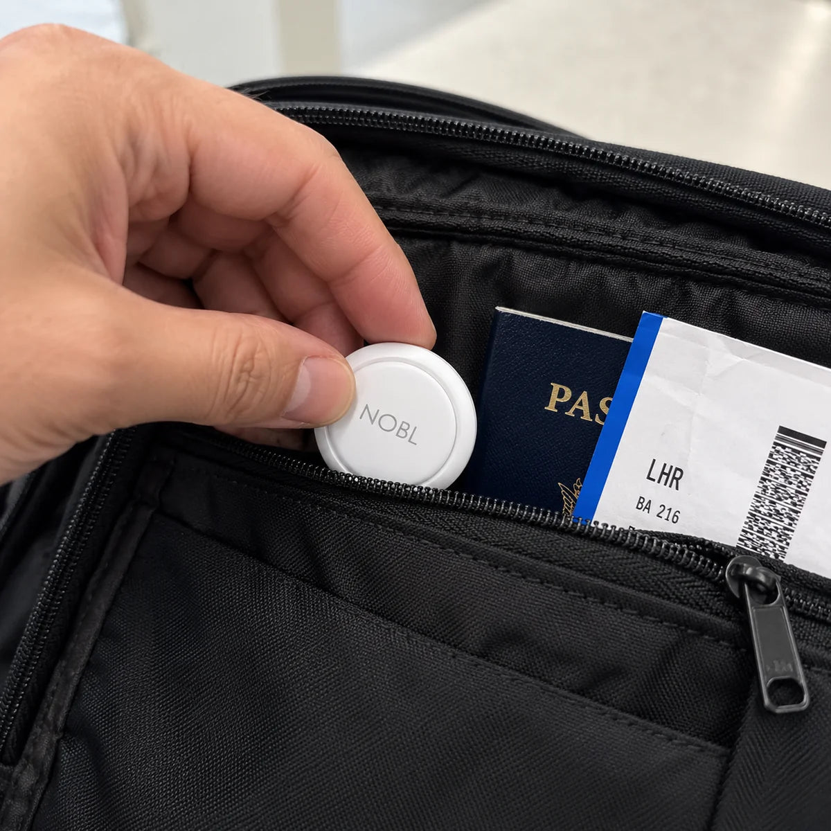 A NOBL Air™ tracker going into a travel bag pocket beside a passport