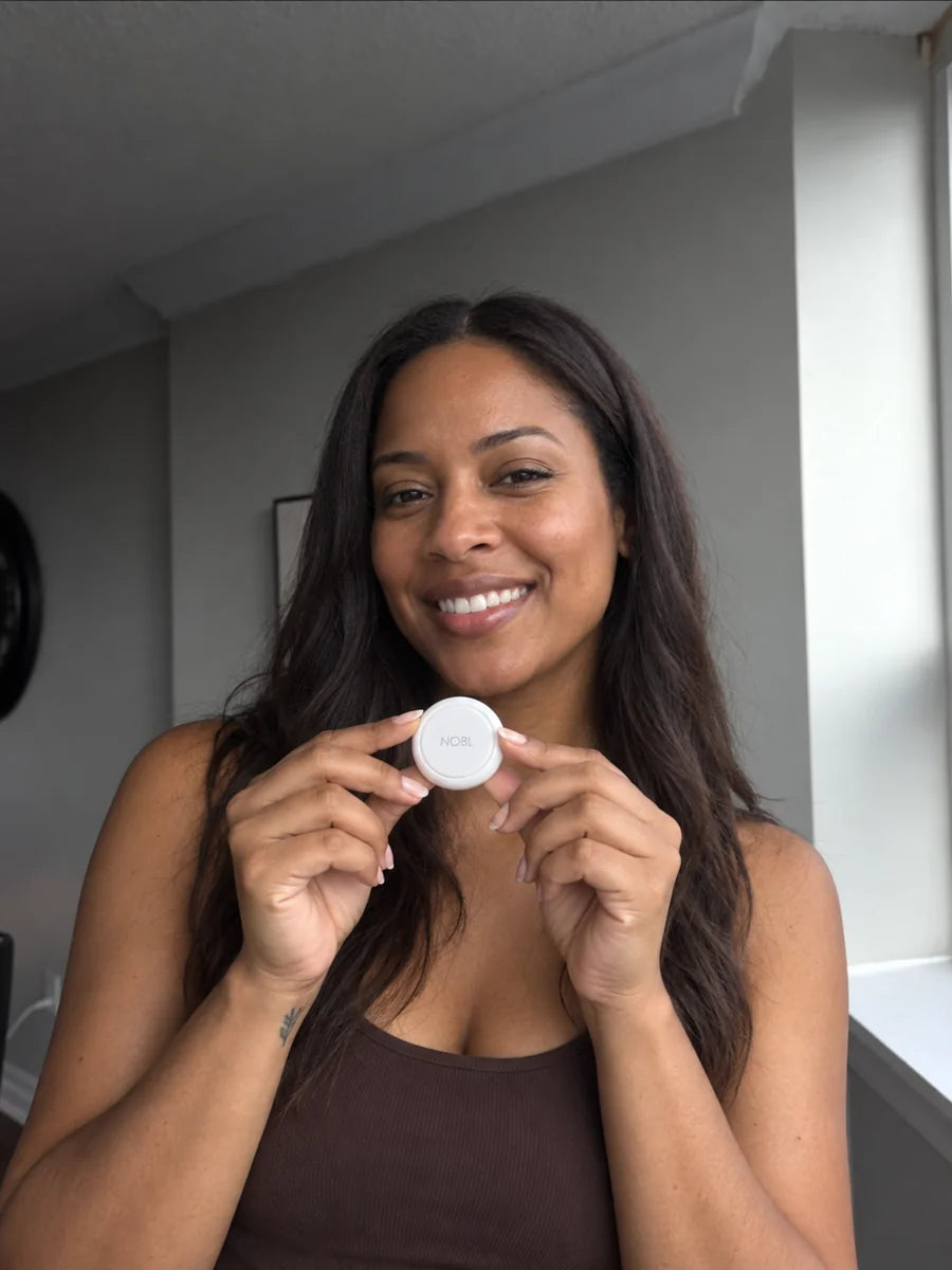 Black woman holding a NOBL Air™ tracker beside a window