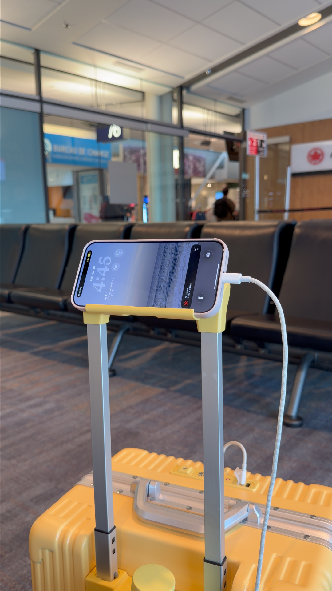 Phone charging from the built-in holder on a yellow NOBL carry-on at the airport