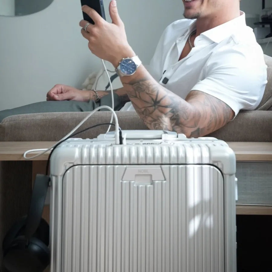 Traveler charging a phone from a silver NOBL carry-on