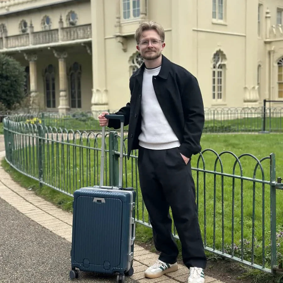 Traveler standing beside a green NOBL carry-on at the Royal Pavilion