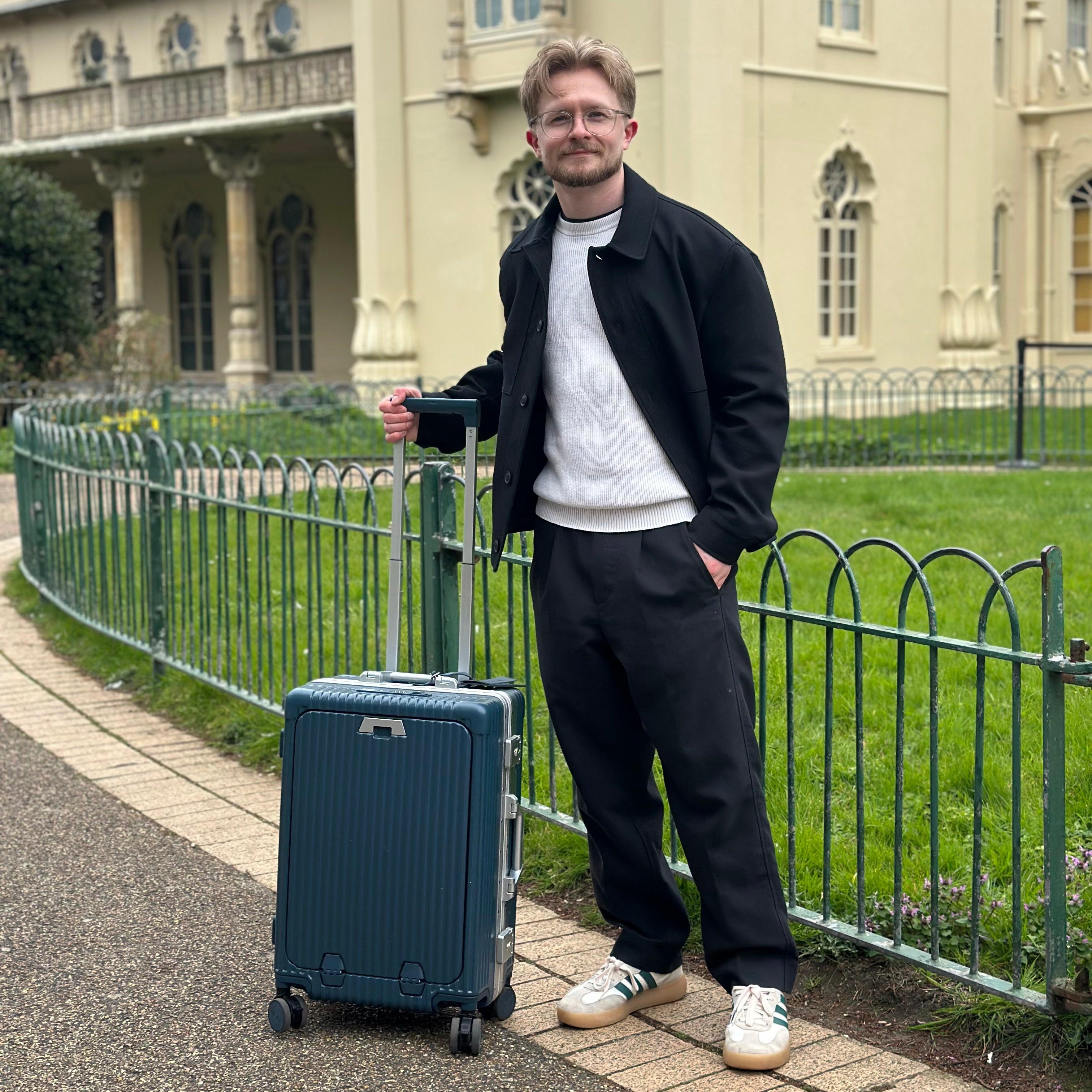 Traveler standing beside a dark NOBL carry-on at the Royal Pavilion
